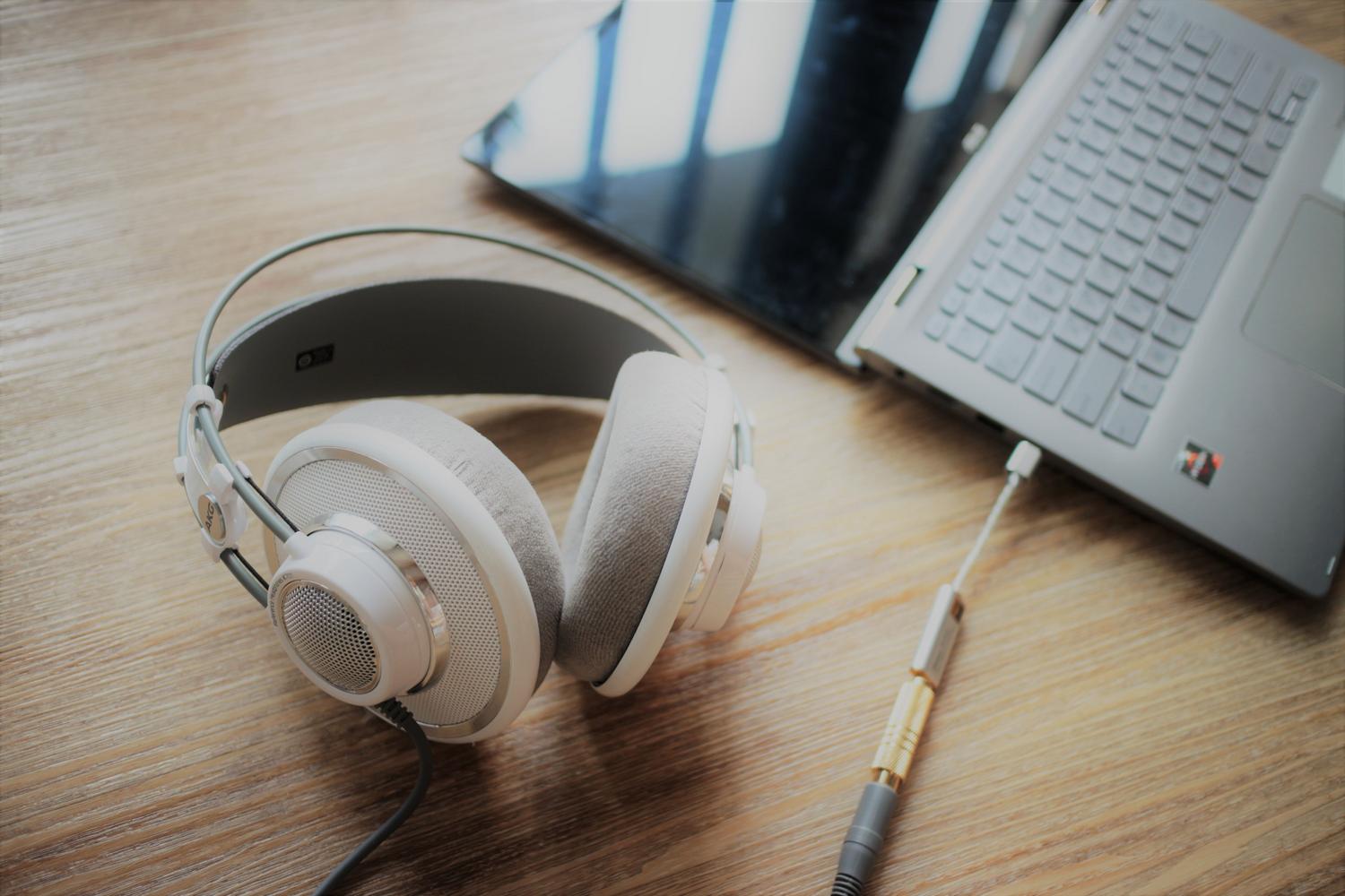Auriculares elegantes conectados a un ordenador portátil sobre una superficie de madera, representando la configuración de audio en Windows.