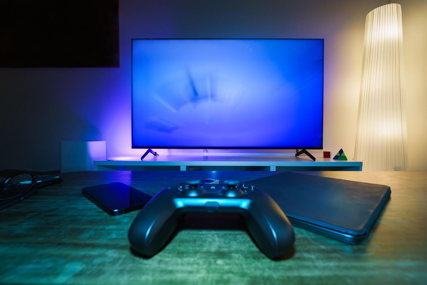 Setup de gaming con consola y mando frente a una televisión con iluminación ambiental, para la sección de ajustes de juego.