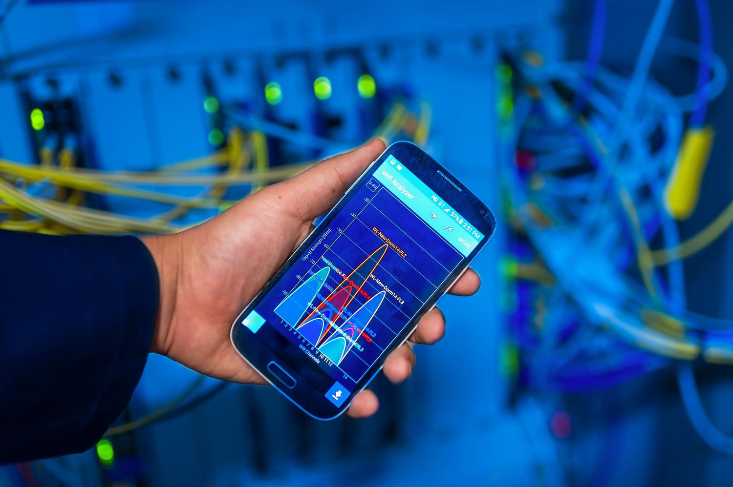 Mano sosteniendo un smartphone que muestra un análisis de red en un entorno de servidores de alta tecnología.