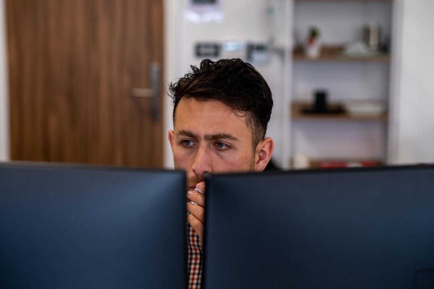 Hombre enfocado en su trabajo utilizando dos monitores en un entorno de oficina.
