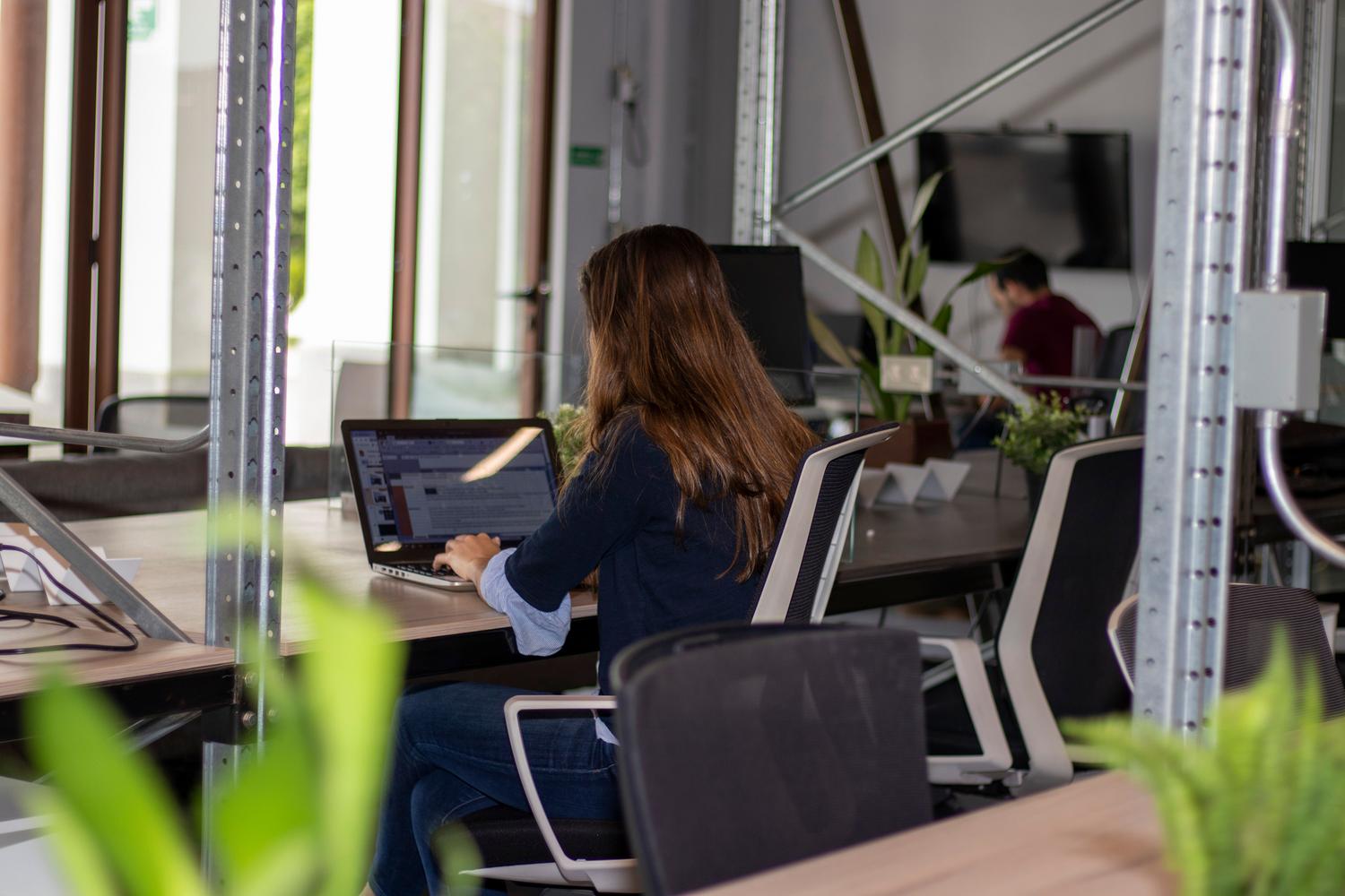 Mujer trabajando con su ordenador portátil en un espacio de coworking luminoso.