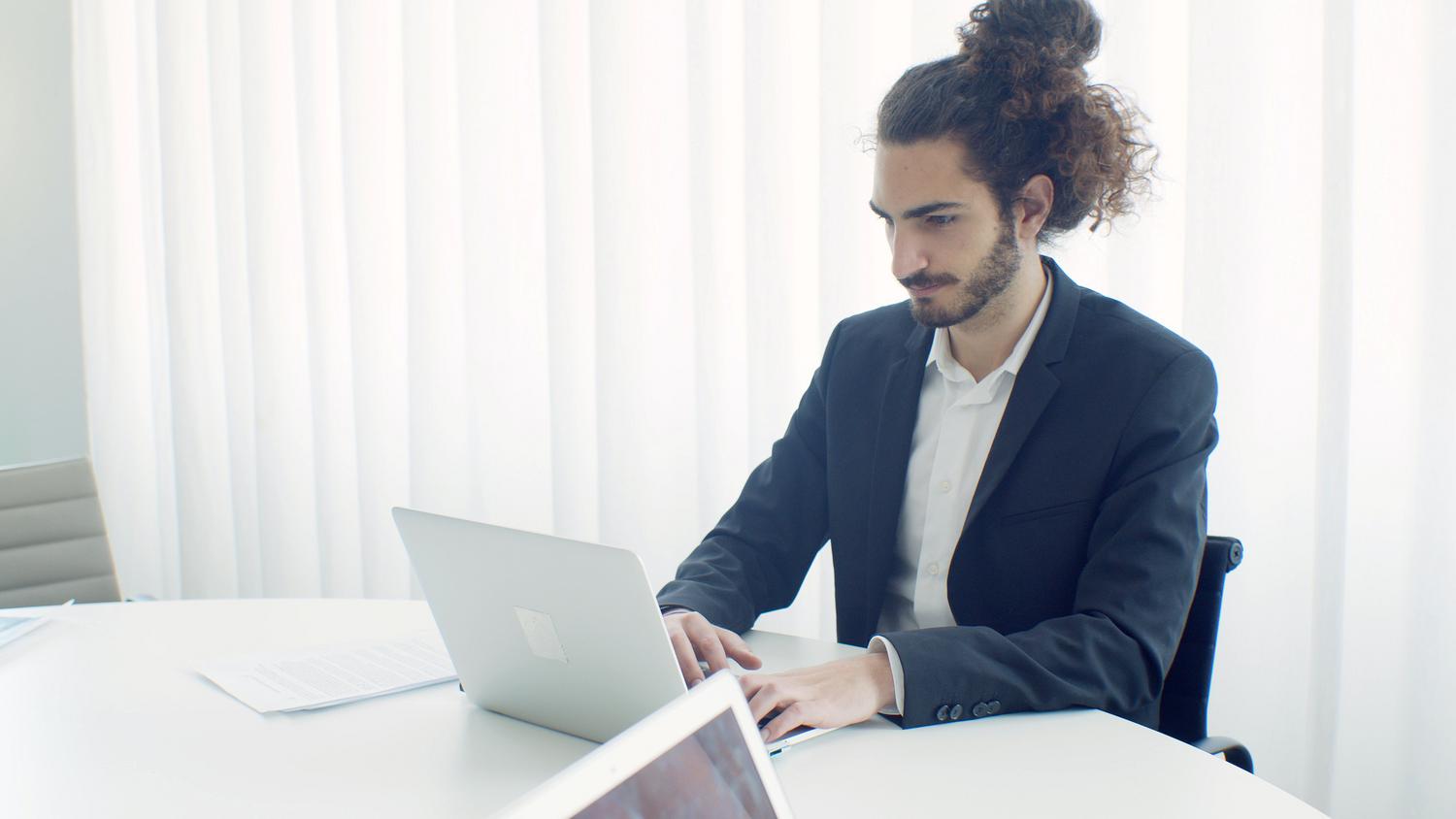 Hombre de negocios trabajando en un portátil dentro de una oficina minimalista y brillante.