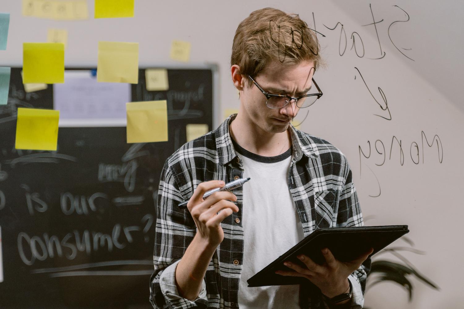 Persona utilizando una tablet frente a un tablero de notas adhesivas y diagramas, simbolizando el modo Canvas de Obsidian.