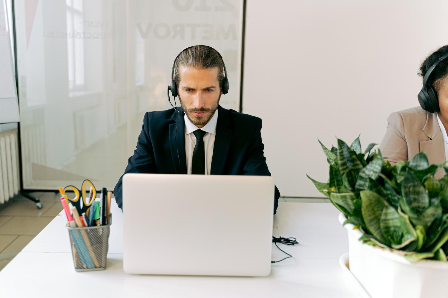 Agente de soporte al cliente utilizando auriculares y portátil en una oficina moderna, ilustrando la optimización del servicio al cliente mediante asistencia de IA.