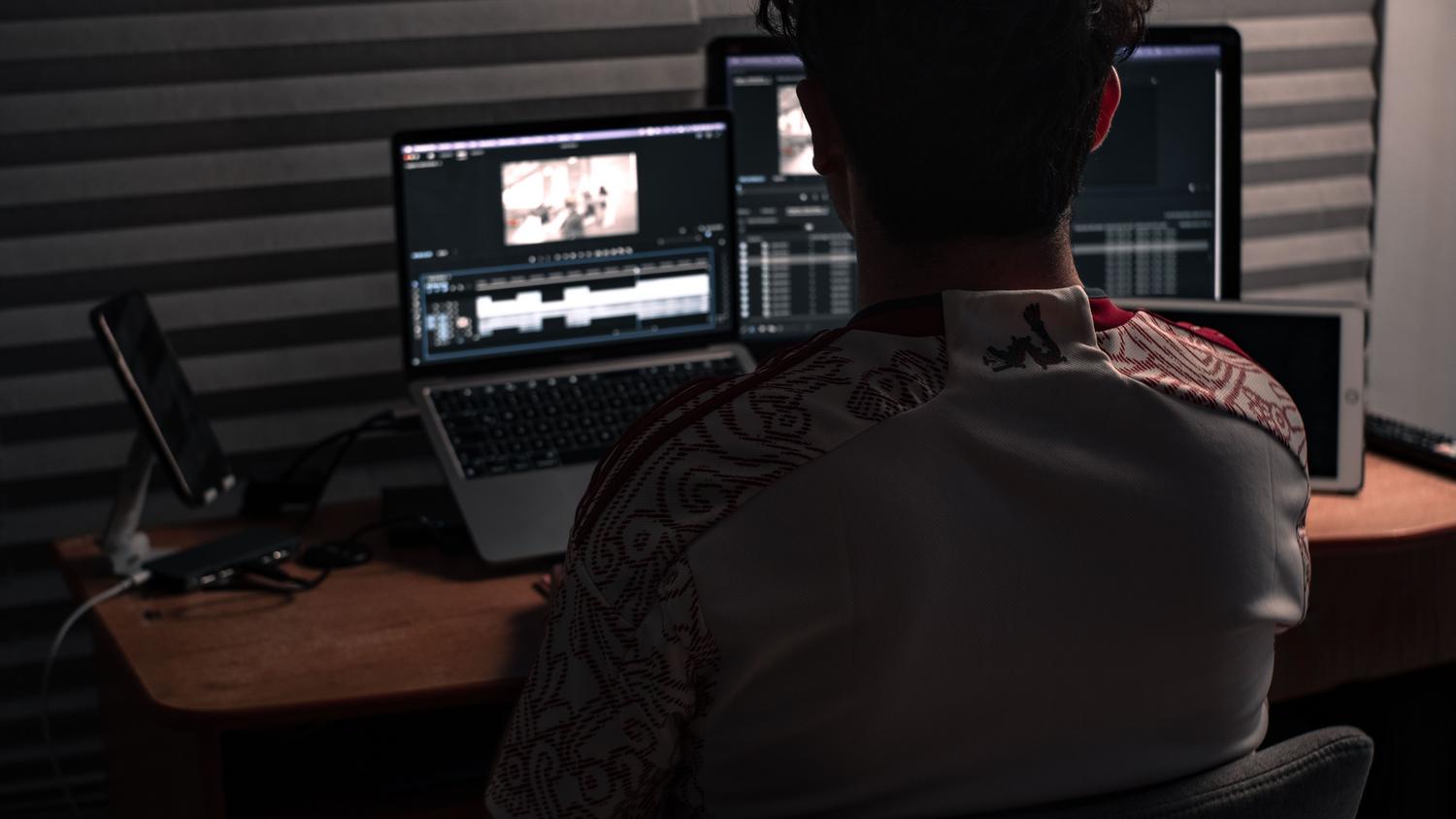 Persona trabajando en la compresión y edición de vídeo utilizando un ordenador portátil y monitores externos en un entorno profesional.