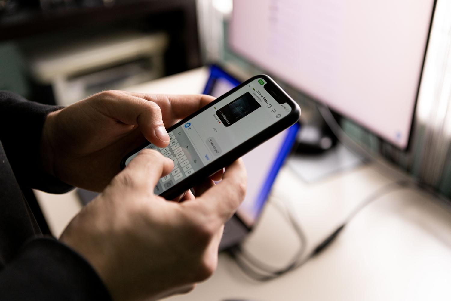 Primer plano de unas manos usando un smartphone frente a la pantalla de un ordenador de escritorio, simbolizando la superposición de tareas digitales y la multitarea.