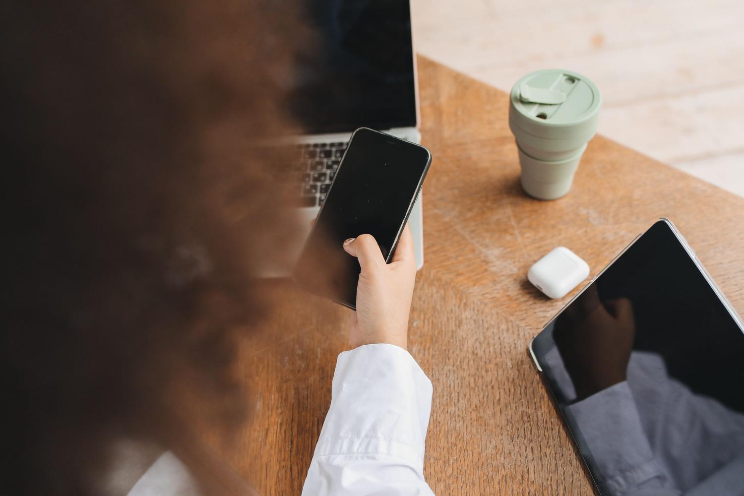 Vista cenital de un espacio de trabajo moderno con un ordenador portátil, un smartphone y una tablet, ilustrando un flujo de trabajo de multitarea con múltiples dispositivos.