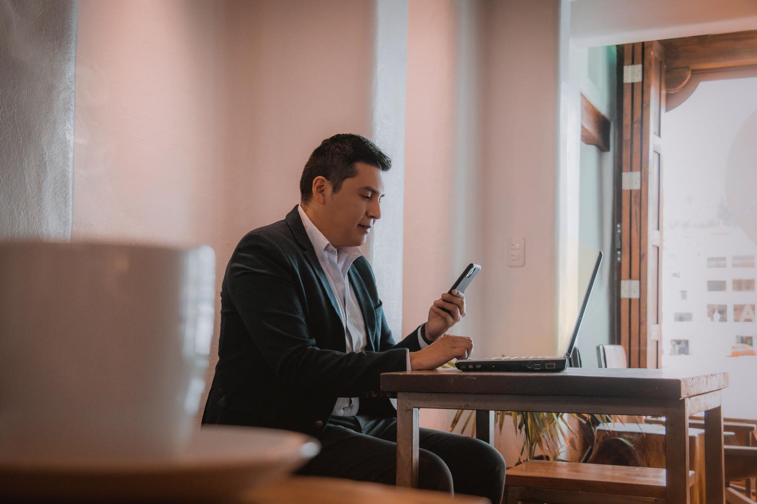 Hombre haciendo multitasking con un ordenador y un móvil en un café, representando el ruido digital y la fragmentación de la atención que los perfiles de concentración resuelven.