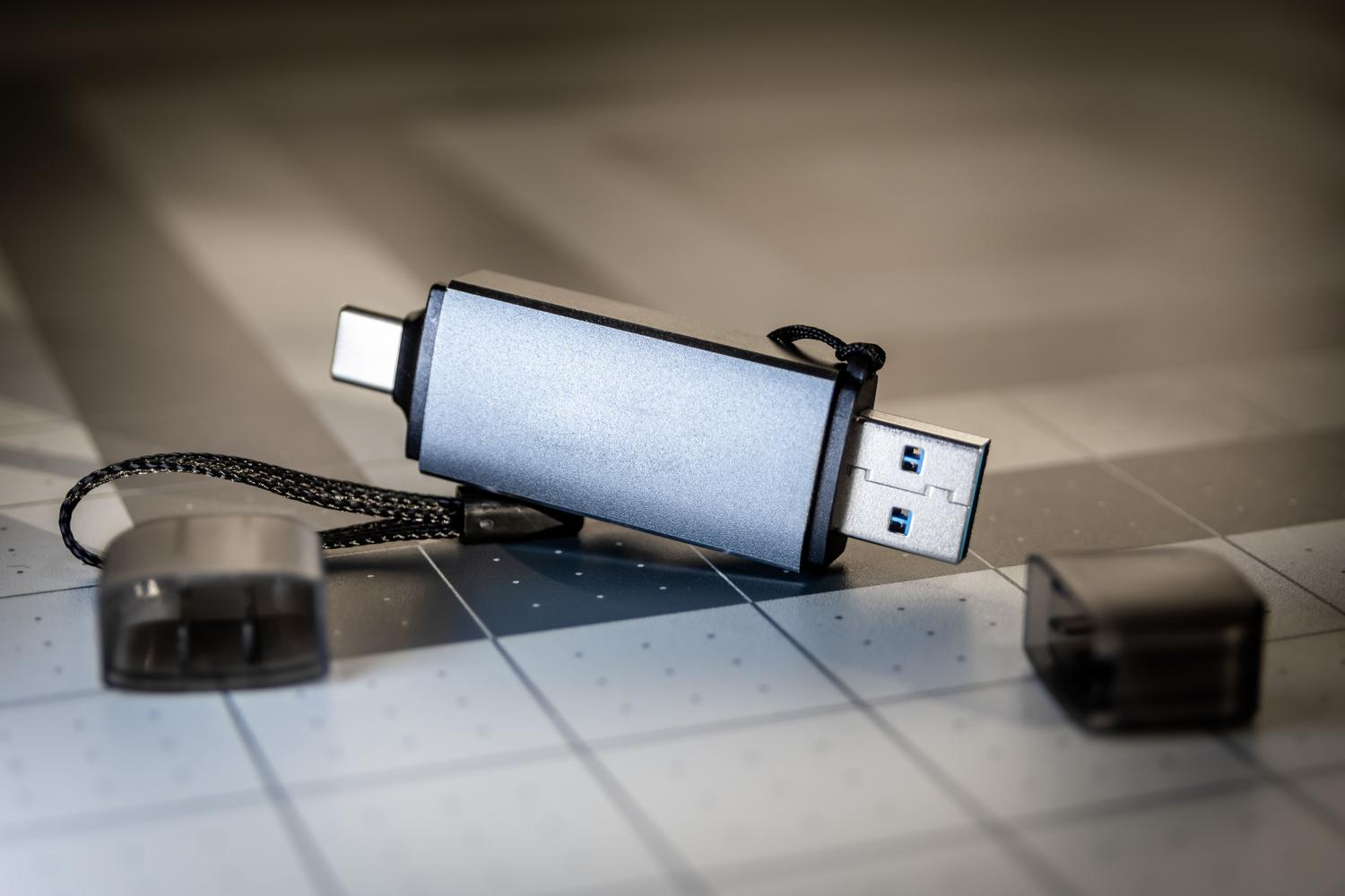 Detaljna fotografija dvostrukog USB flash pogona (USB-A i USB-C) na rešetkastoj tehničkoj površini, s istaknutim konektorima.
