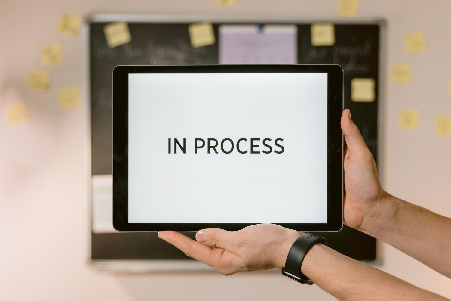 Tablet mostrando el estado 'IN PROCESS' en un entorno de oficina con notas adhesivas, ilustrando la gestión y automatización de flujos de trabajo.
