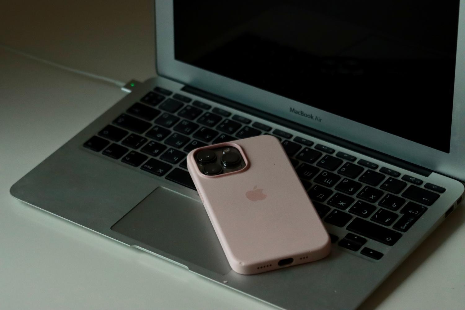 iPhone apoyado sobre el teclado de un MacBook, ilustrando la importancia de mantener los equipos cerca para una conexión estable.