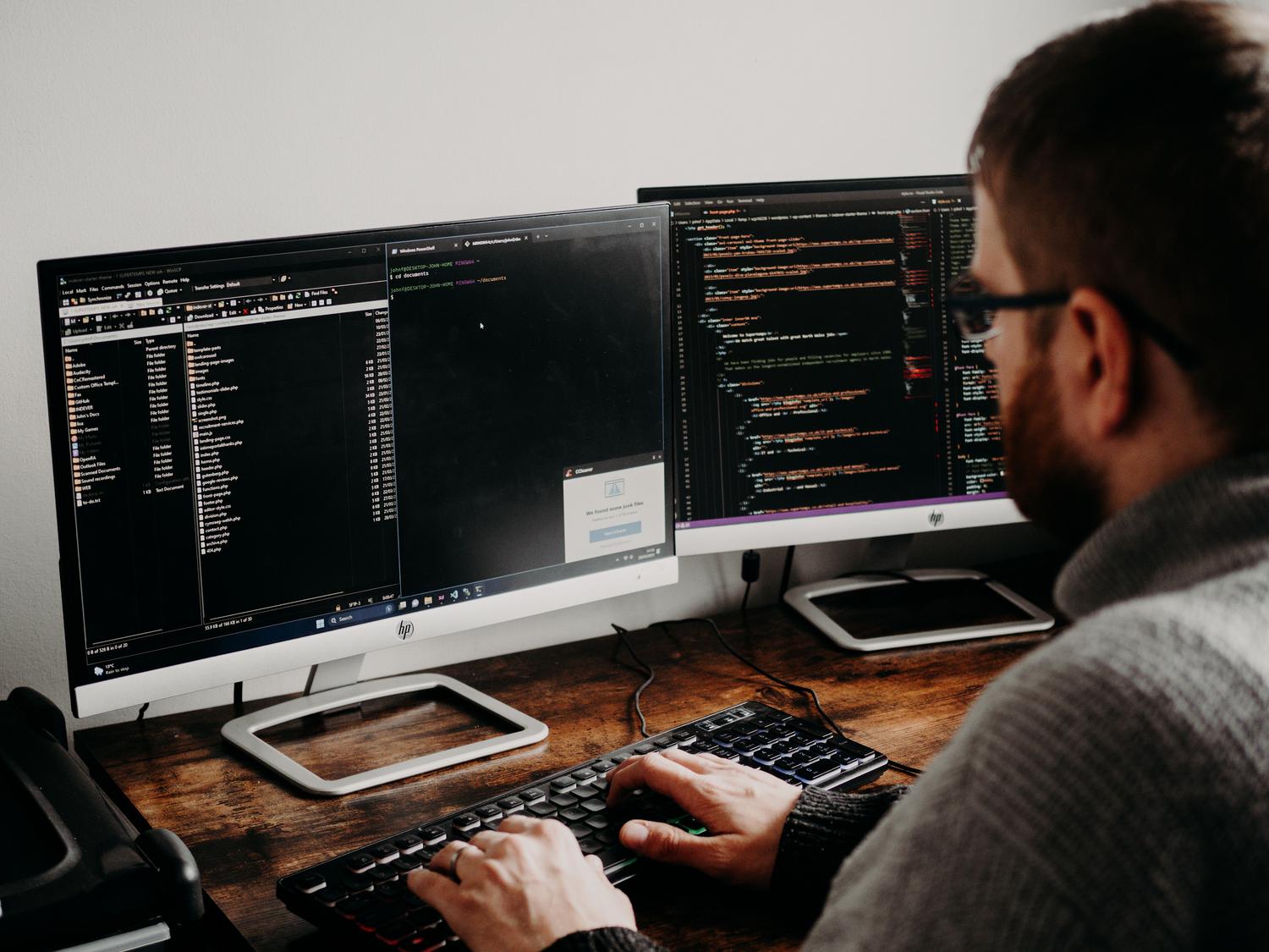 Desarrollador de software escribiendo scripts de automatización en Windows PowerShell utilizando monitores duales