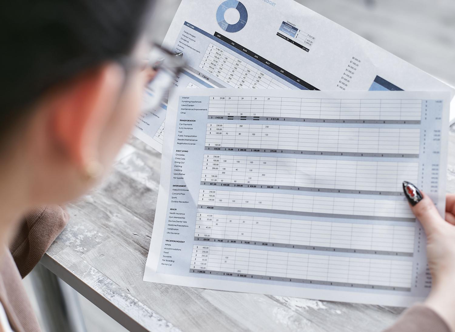 Mujer de negocios analizando hojas de cálculo financieras con gráficos en una oficina, reflejando el profesionalismo y la seriedad de los informes administrativos.