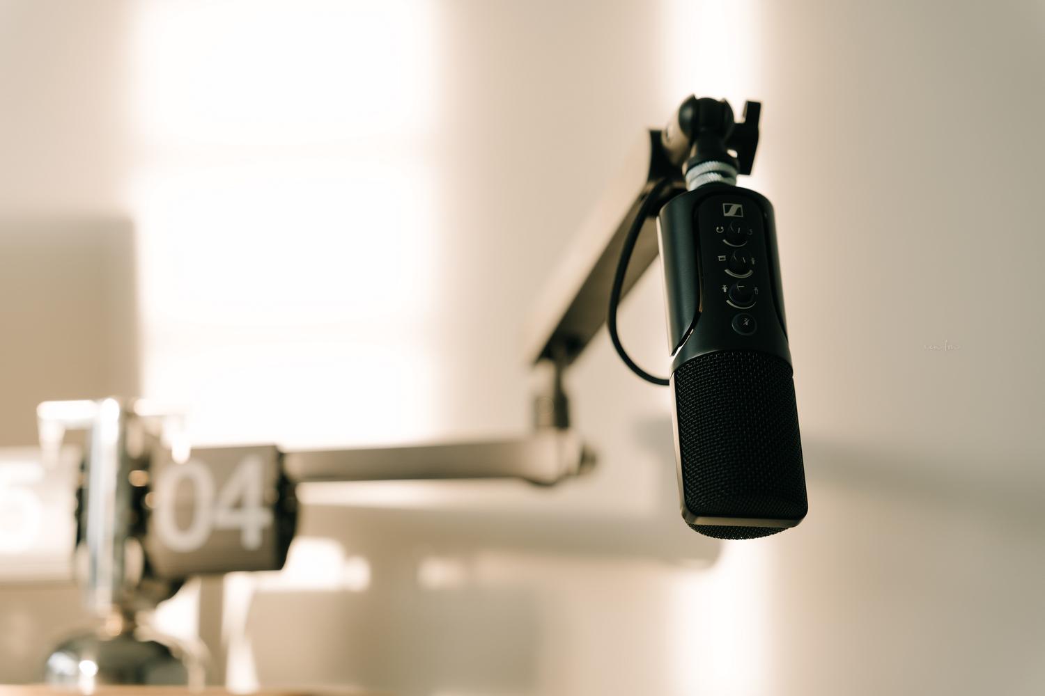 Primer plano de un micrófono profesional de condensador en un brazo articulado dentro de un estudio de podcast minimalista.