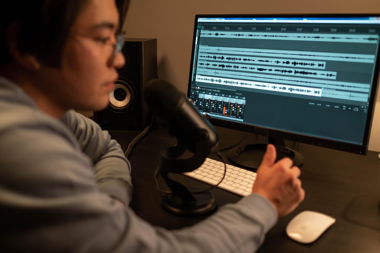Editor de sonido concentrado trabajando en la limpieza de pistas de audio en un monitor de computadora.