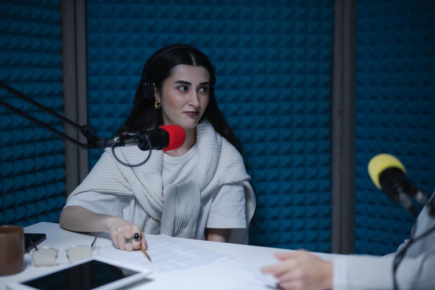 Mujer grabando un episodio de podcast en un estudio profesional con paneles acústicos y auriculares.