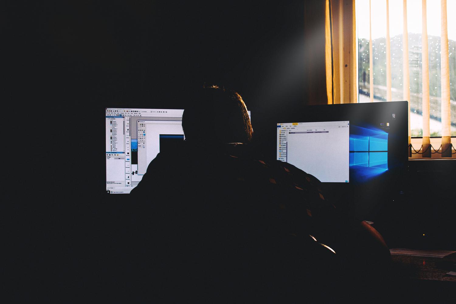 Persona trabajando en una oficina oscura con monitores, representando el problema del parpadeo de pantalla o flickering.
