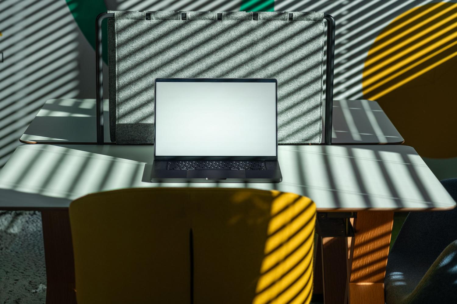 Laptop sobre un escritorio con luz natural y sombras de persianas, ilustrando el funcionamiento del sensor de luz ambiental (ALS).
