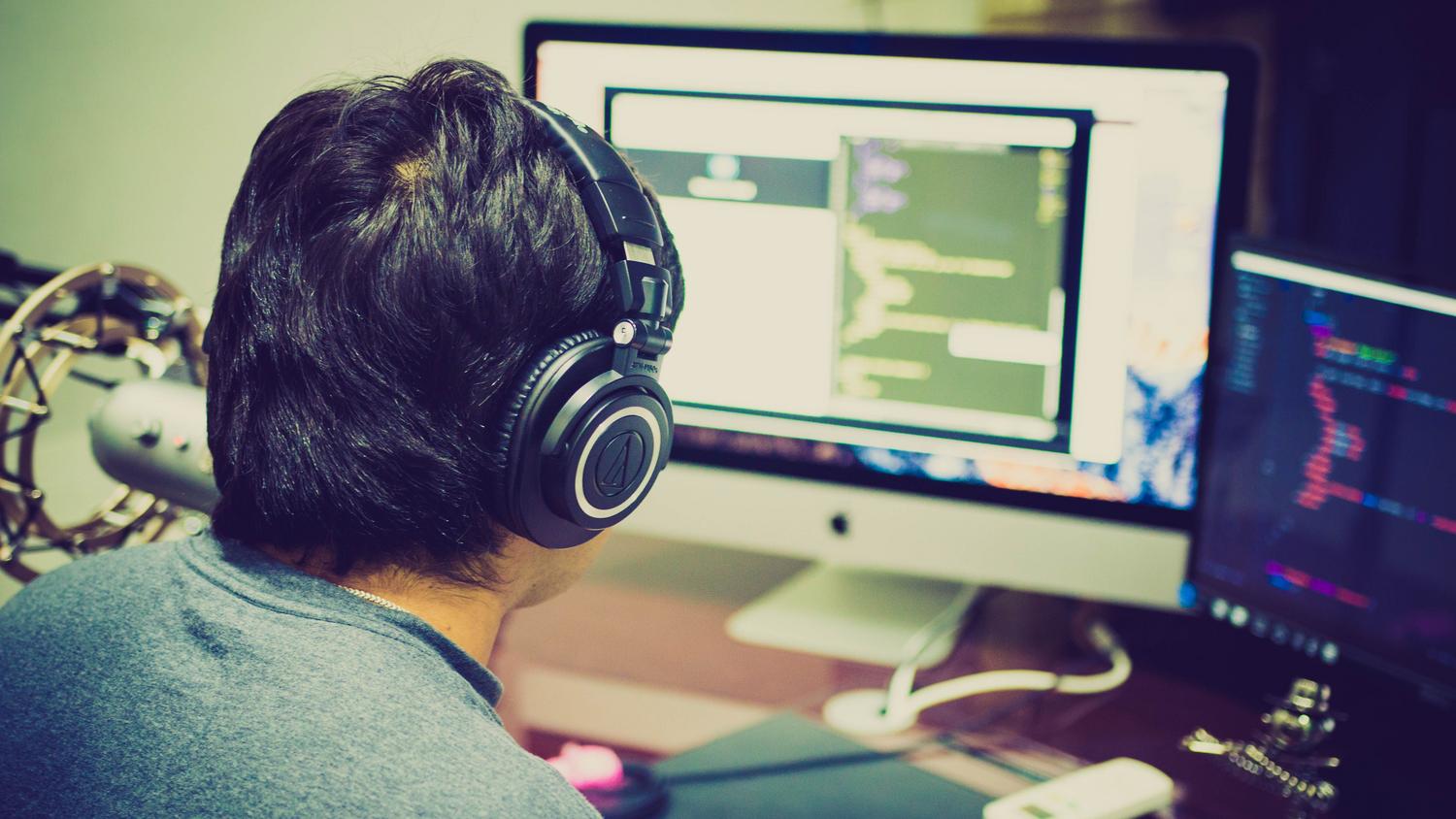 Programador concentrado usando auriculares y doble monitor para optimizar su flujo de trabajo.
