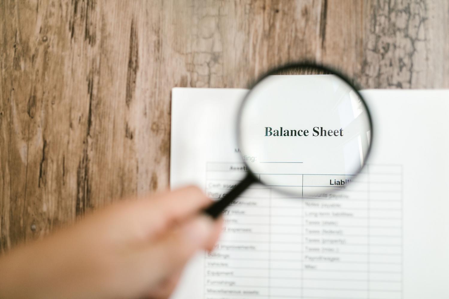 Traditional credit risk review showing a human hand using a magnifying glass to analyze a company balance sheet