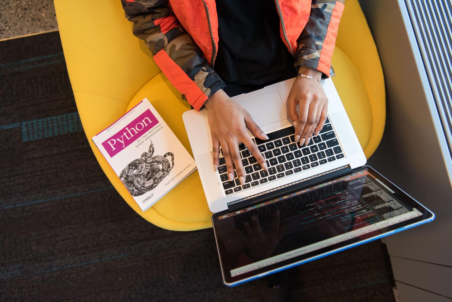 Una desarrolladora programando en un portátil con un libro de Python al lado, representando el aprendizaje y desarrollo de IA. Una desarrolladora programando en un portátil con un libro de Python al lado, representando el aprendizaje y desarrollo de IA.
