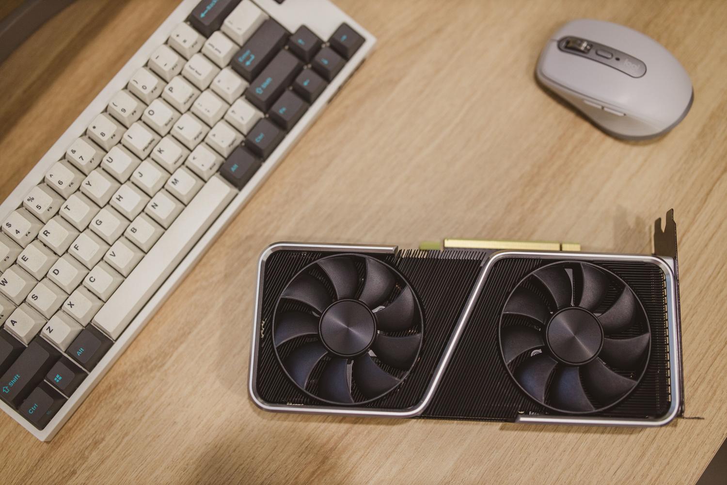 Vista cenital de un escritorio con una tarjeta gráfica GPU, teclado y ratón, ilustrando el hardware necesario para el procesamiento de IA en casa.