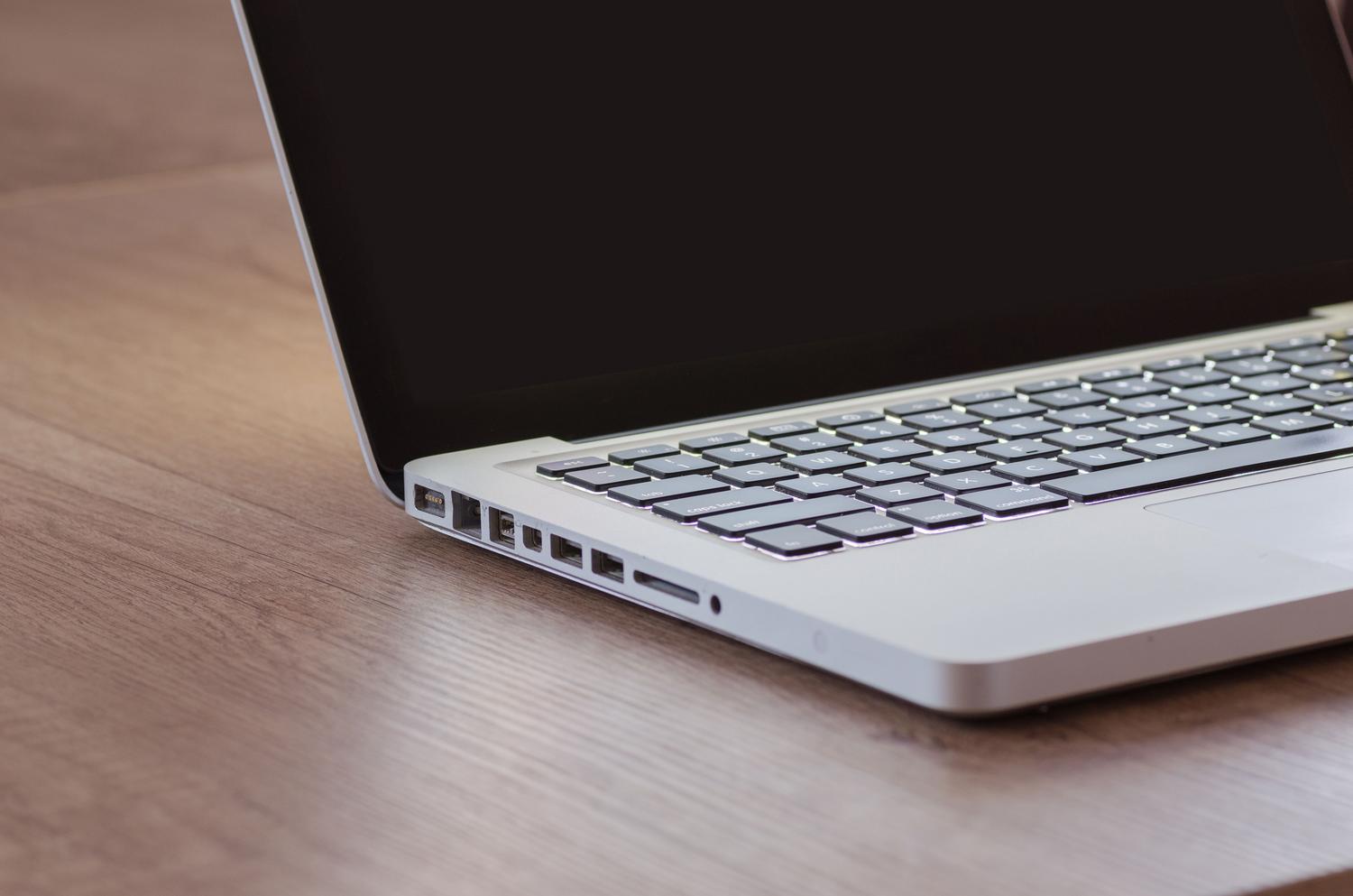Primer plano de un ordenador portátil moderno con teclado retroiluminado sobre un escritorio de madera, evocando un entorno de trabajo técnico.