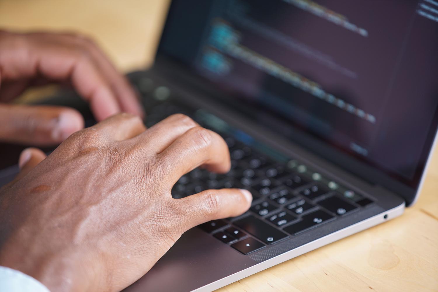 Primer plano de manos escribiendo en un teclado de portátil con una pantalla de código desenfocada, representando la configuración técnica en una terminal de Linux.