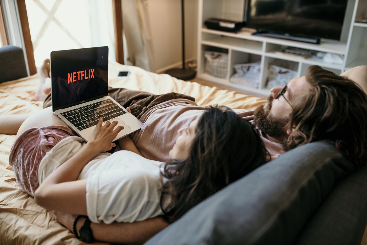 Pareja relajándose cómodamente mientras disfrutan de contenido multimedia en un portátil.