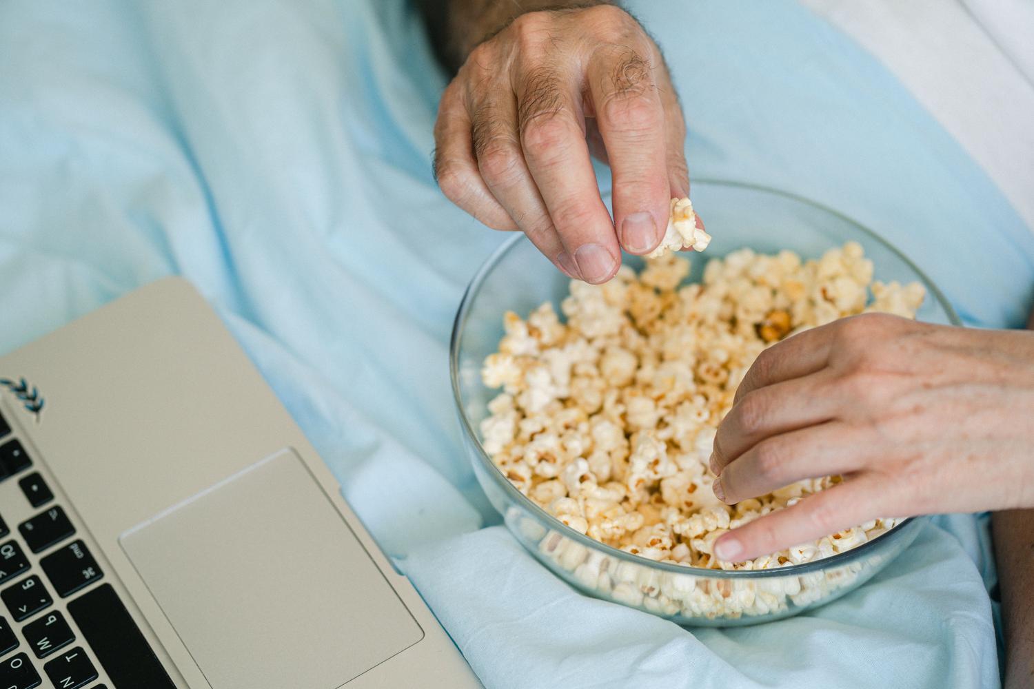 Momento acogedor de noche de cine en casa con un ordenador portátil y un bol de palomitas.