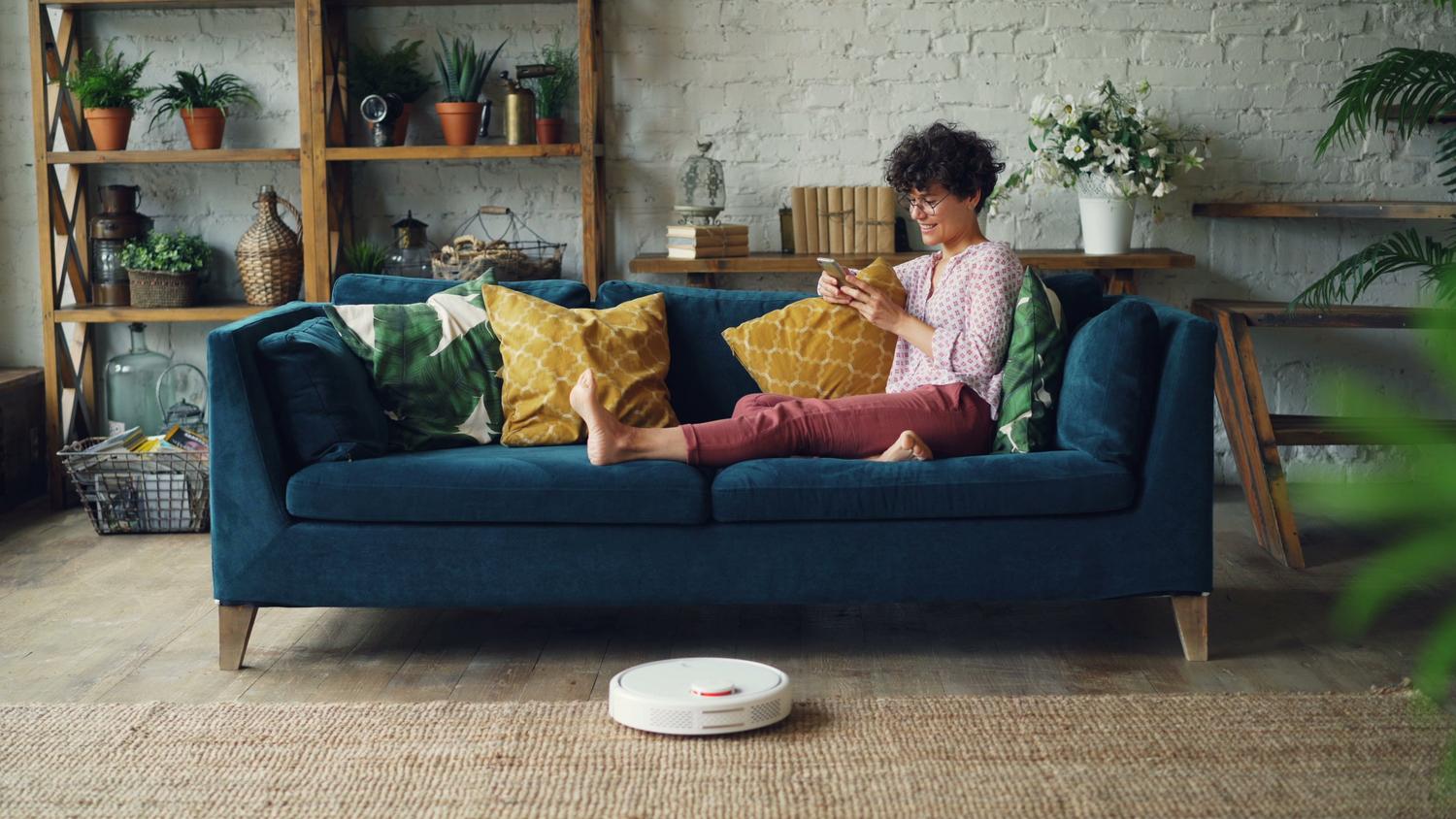 Persona controlando la limpieza de su hogar con un robot aspirador desde el sofá