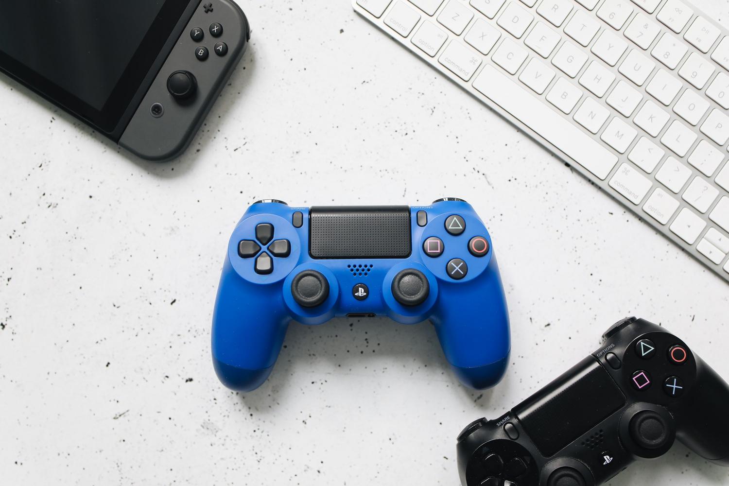 Vista superior de diversos mandos de videojuegos y un teclado sobre una superficie blanca, ilustrando la variedad de dispositivos y tecnologías.
