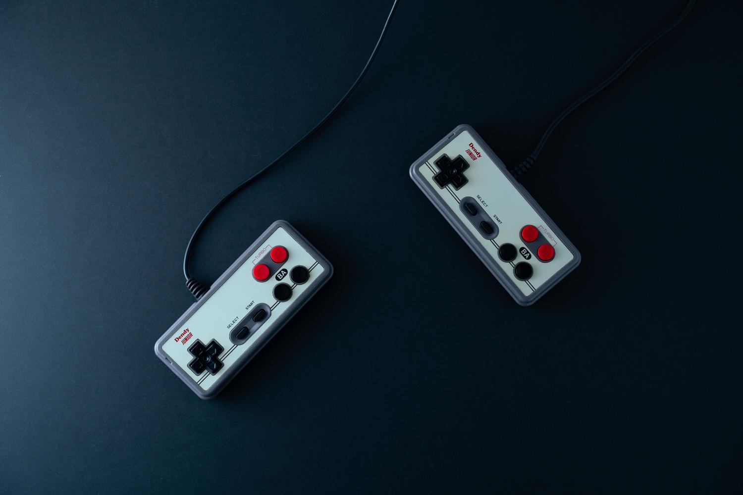 Dos mandos de estilo retro Dendy/NES sobre una superficie oscura, ideales para ilustrar la nostalgia y el uso de emuladores de consolas clásicas.