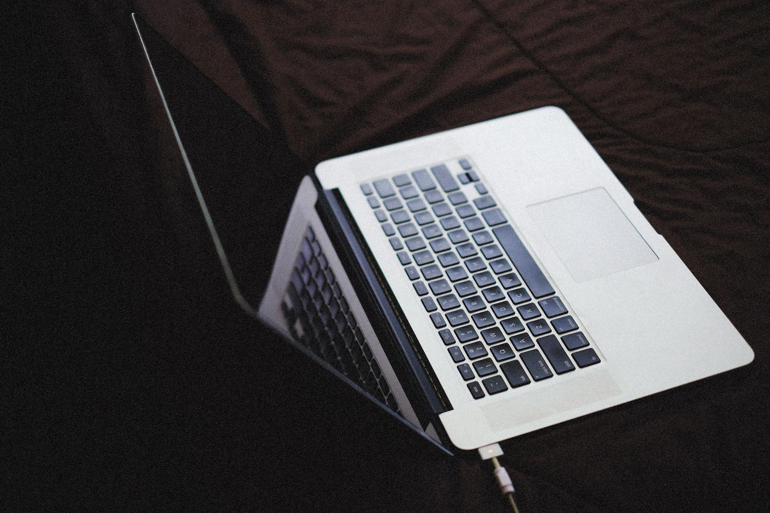Laptop conectado a un cargador sobre una superficie oscura, representando la recarga de la batería.