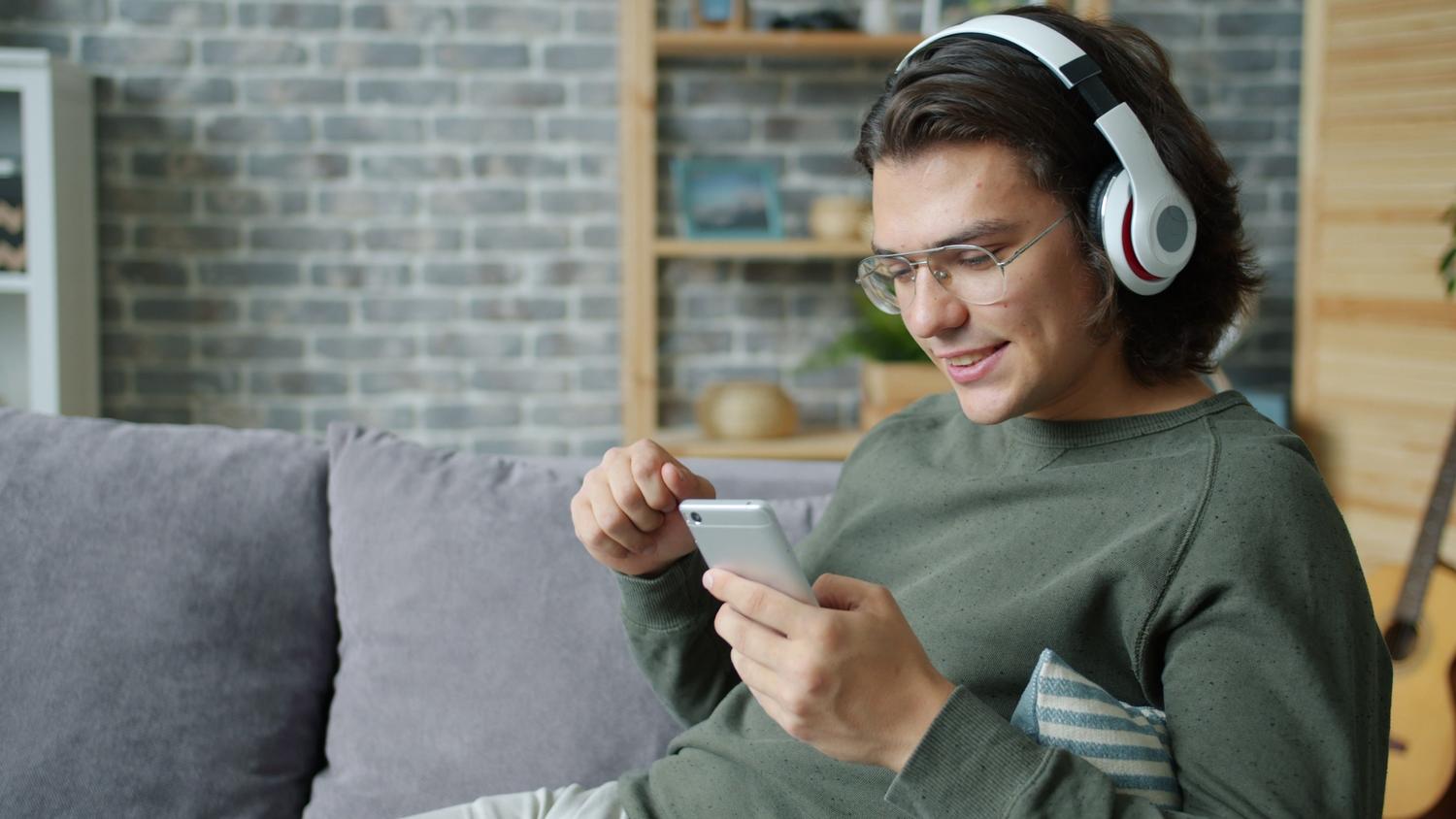 Hombre joven relajado en un sofá escuchando música con auriculares y un smartphone Hombre joven relajado en un sofá escuchando música con auriculares y un smartphone