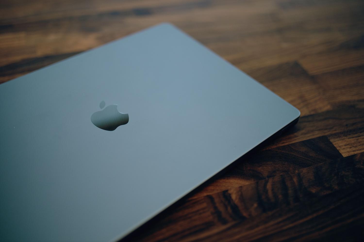 MacBook plateada cerrada sobre una mesa de madera oscura con iluminación suave, proporcionando una estética profesional para tutoriales técnicos.