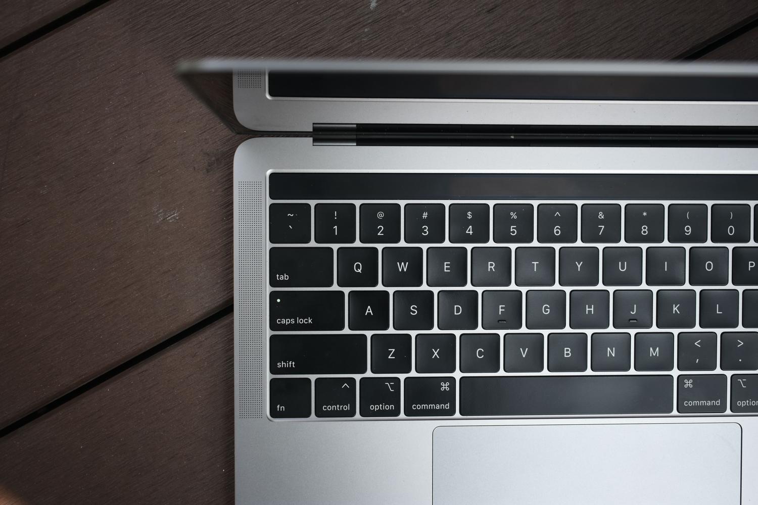 Vista cenital de un teclado de MacBook Pro sobre una superficie de madera oscura, representando un espacio de trabajo limpio y productivo.