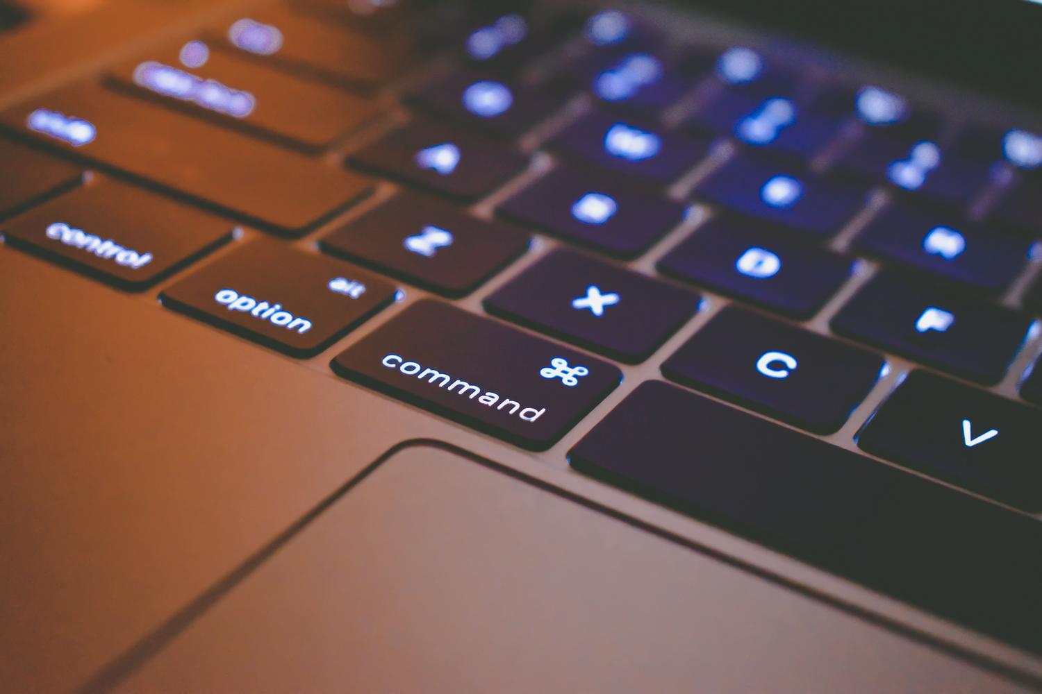 Plano detalle de las teclas de comando y opción de un teclado de MacBook con retroiluminación, resaltando la eficiencia y los atajos de teclado.
