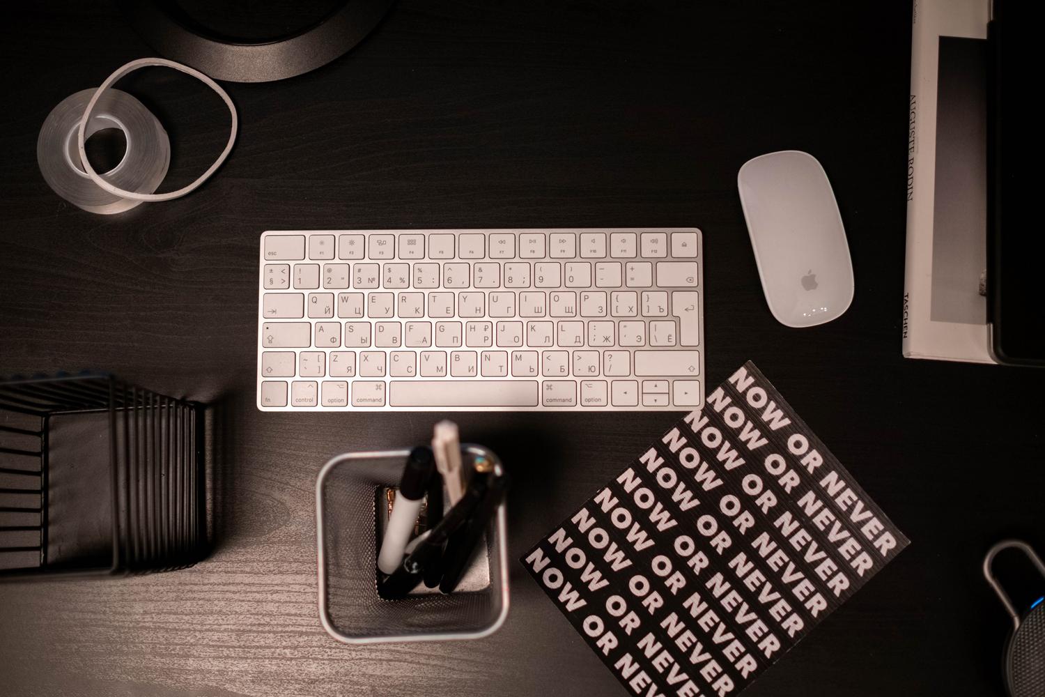 Composición flat lay de un teclado Apple Magic Keyboard y ratón en un escritorio oscuro con elementos creativos y motivadores.