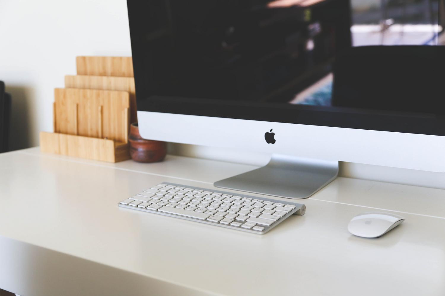 Espacio de trabajo minimalista con un iMac, teclado y ratón inalámbricos sobre un escritorio blanco y luminoso.