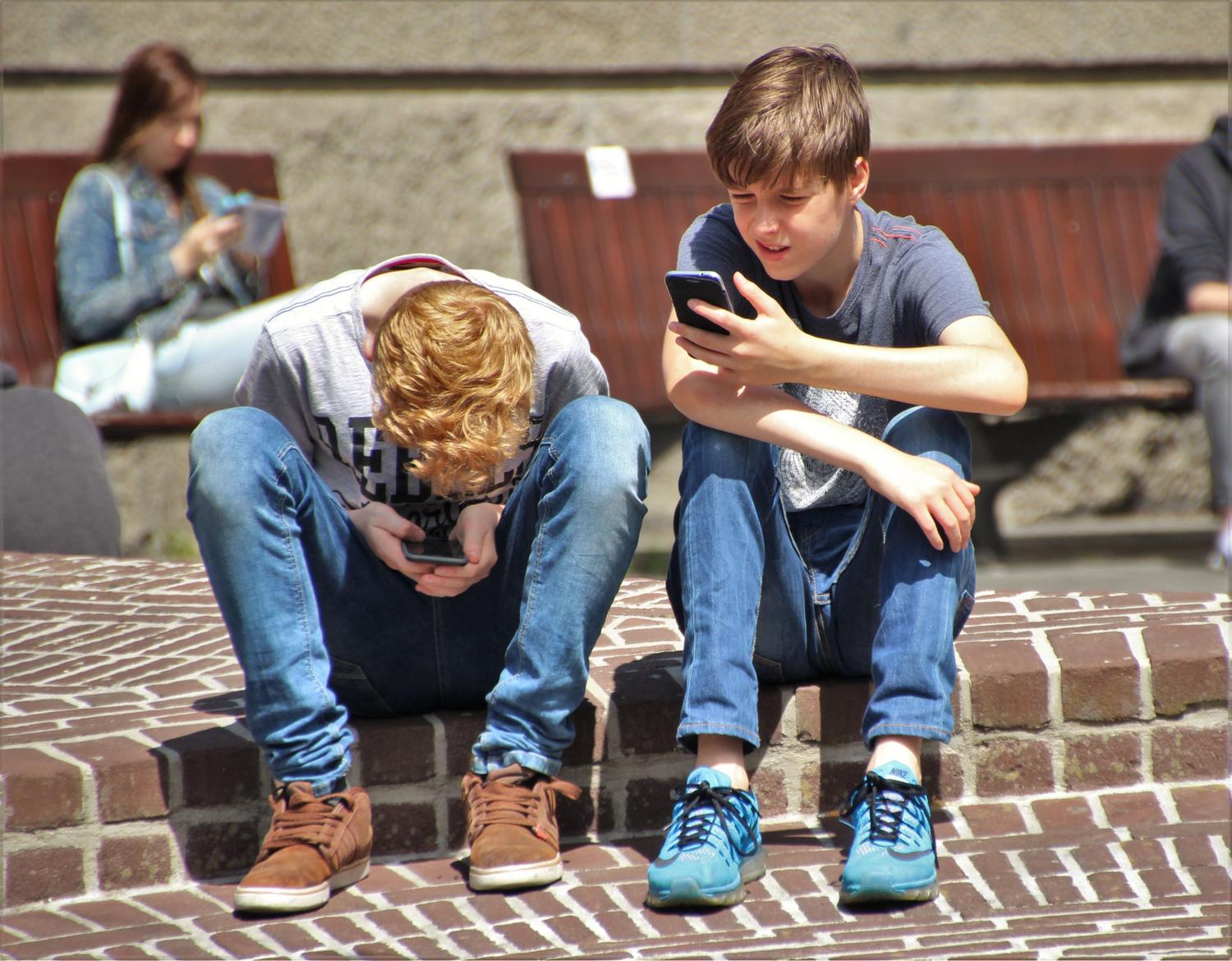 Dos adolescentes absortos en sus teléfonos móviles, representando el aislamiento digital y la adicción a las redes sociales.
