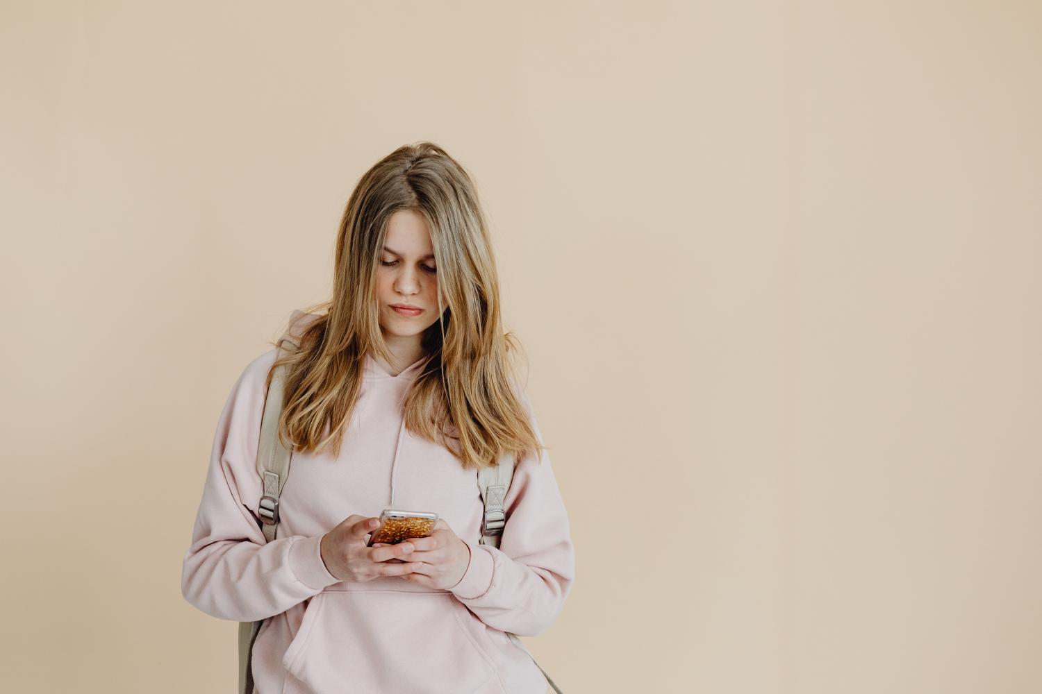 Una adolescente con mochila utilizando su smartphone, ilustrando la vulnerabilidad de los menores ante la privacidad en línea.