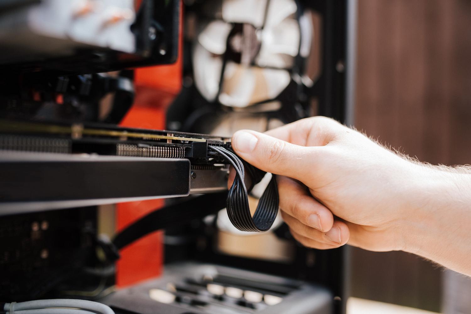 Primer plano de una mano conectando el cable de alimentación a una tarjeta gráfica GPU dentro de la torre de un PC.