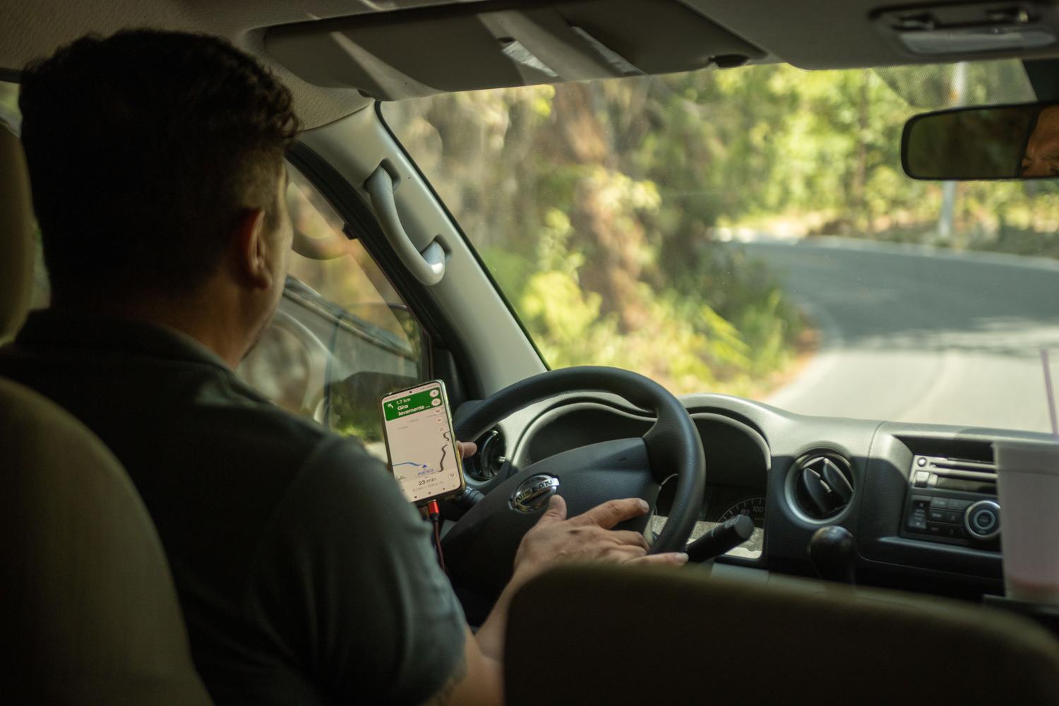 Conductor utilizando una app de GPS en una carretera sinuosa rodeada de árboles, ejemplificando las interferencias ambientales en la precisión del GPS.