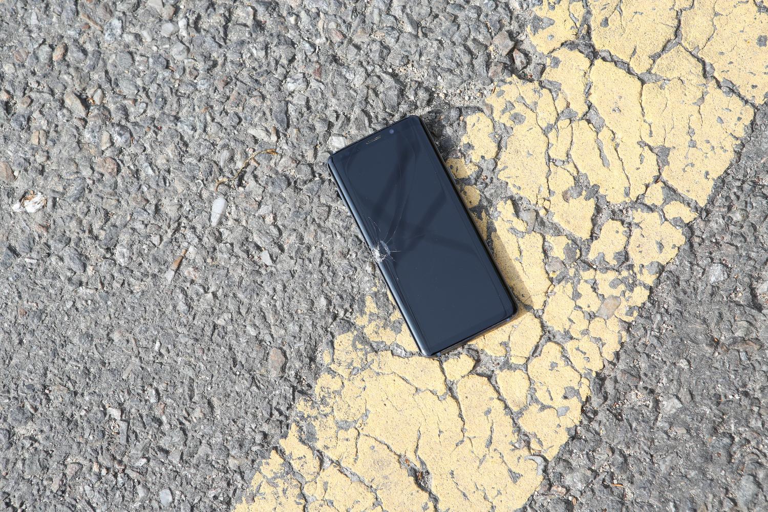 Smartphone con la pantalla destrozada caído sobre el asfalto, representando un accidente común.