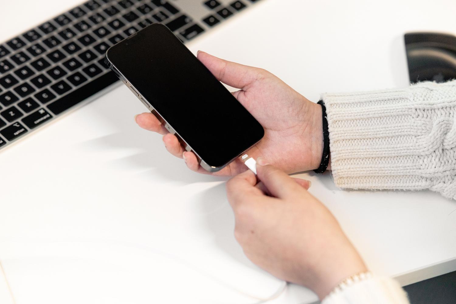 Persona conectando un teléfono móvil a un ordenador en un escritorio, ilustrando el proceso de conectar el dispositivo para usar iTunes o Finder.