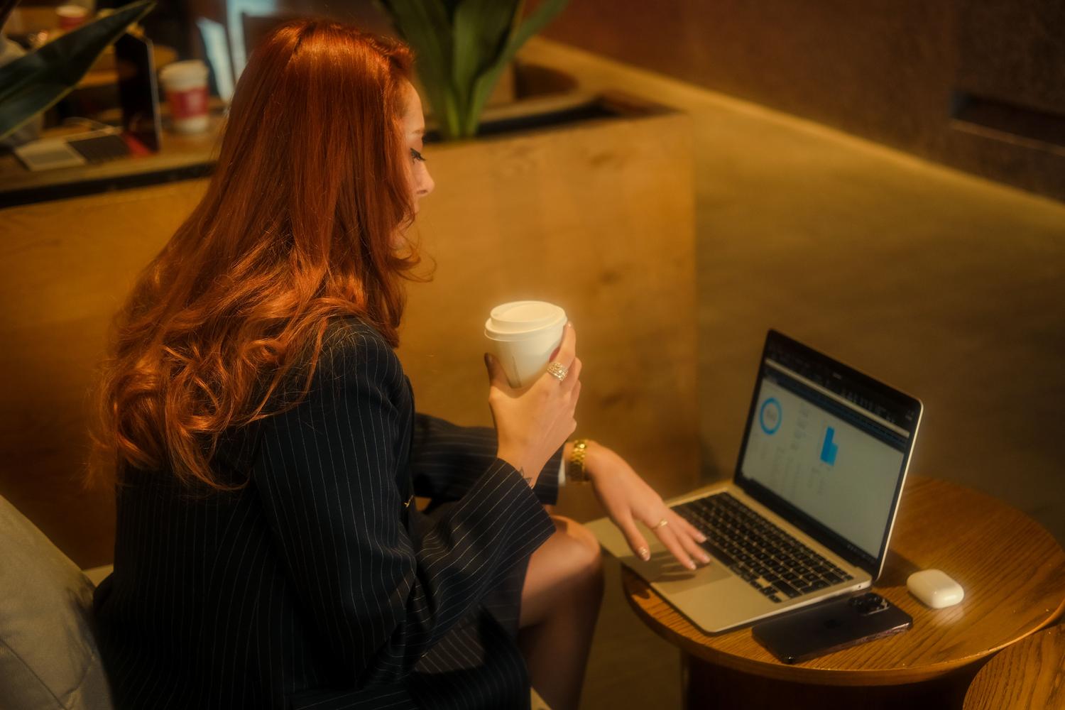 Una mujer trabajando con su portátil en una cafetería, representando la necesidad de optimizar la batería cuando se trabaja en movilidad sin cargador.