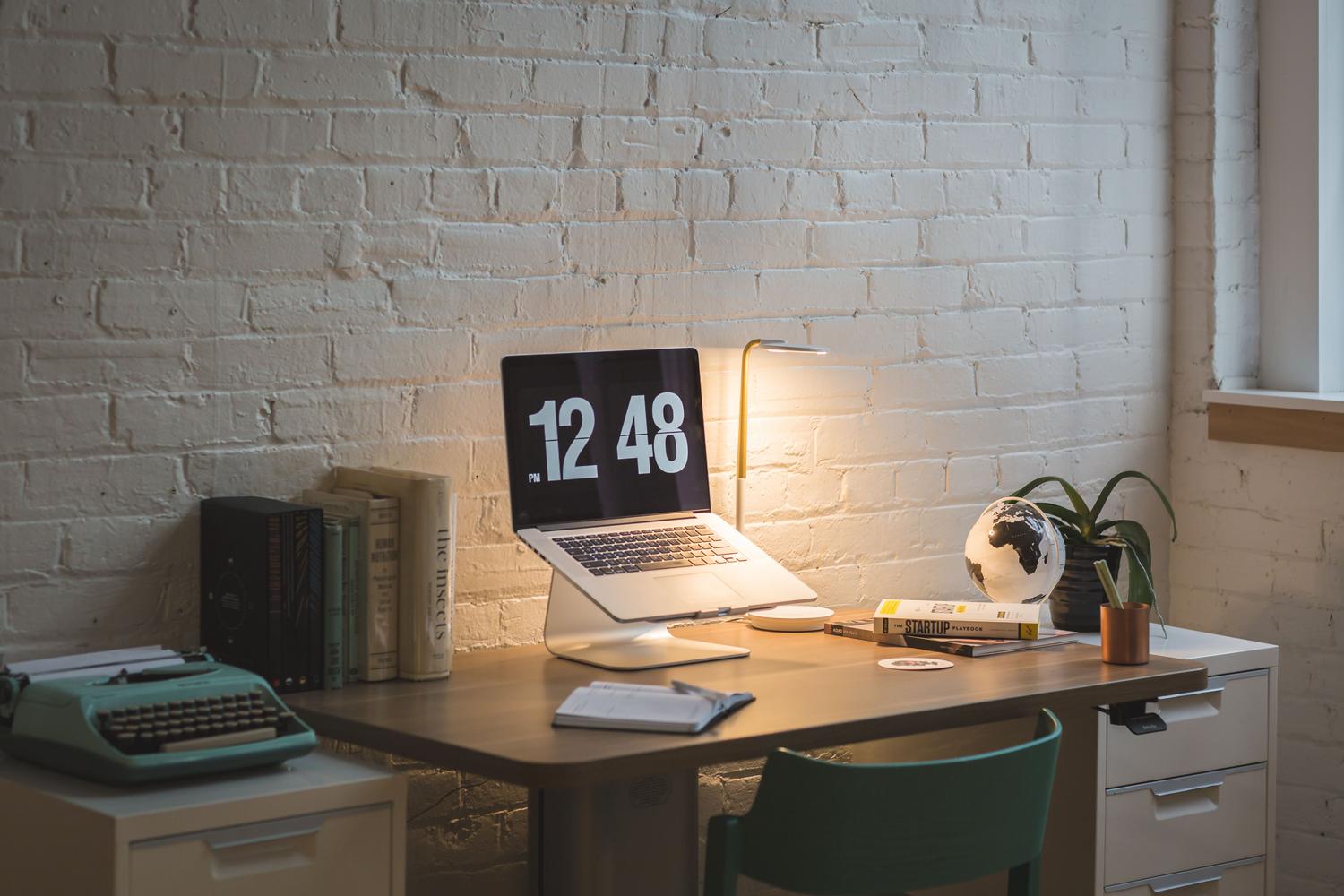 Mesa de trabajo organizada con MacBook, libros y lámpara, ejemplificando un entorno de trabajo fluido.