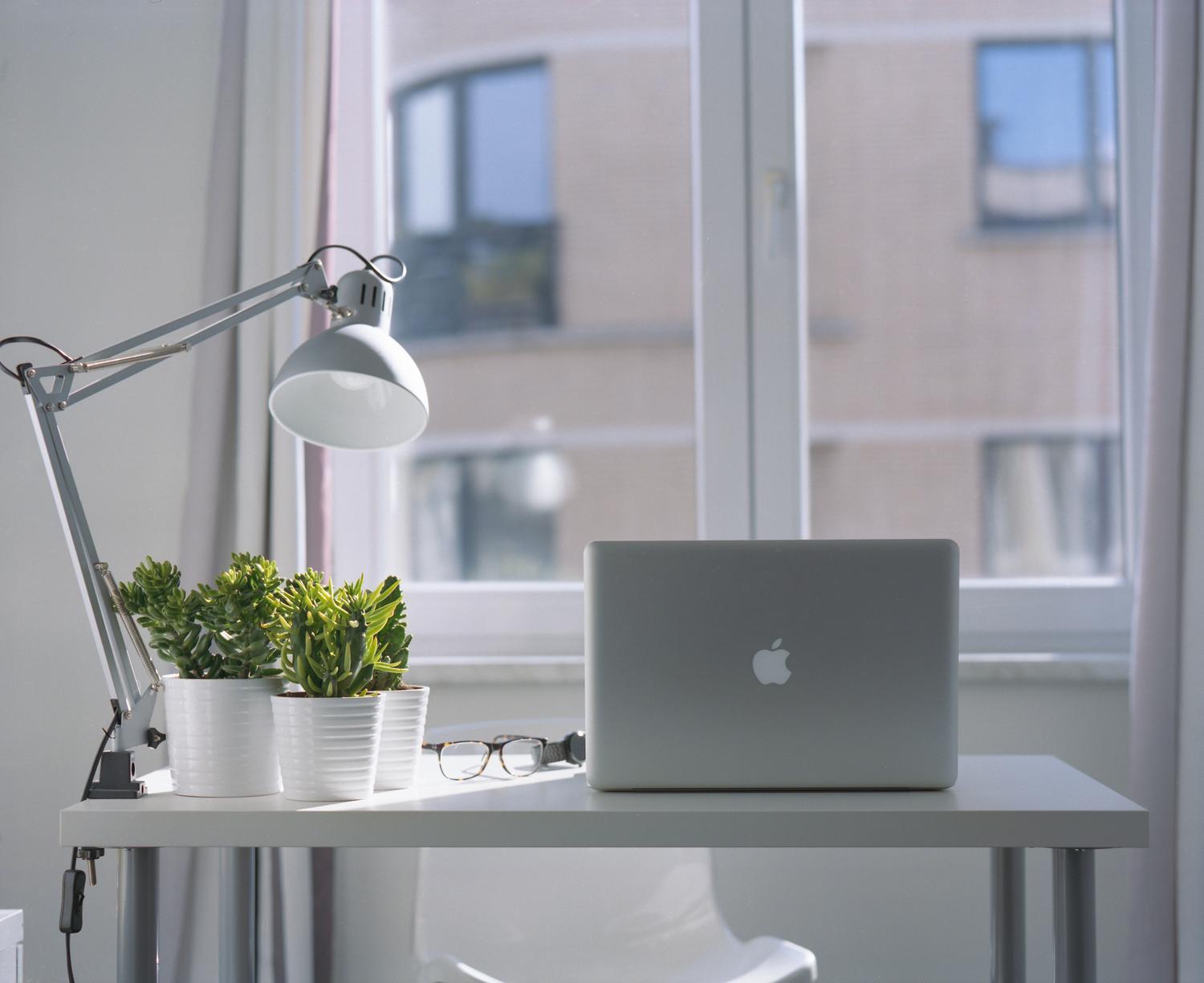 Espacio de trabajo luminoso y moderno con MacBook y plantas, evocando un entorno de trabajo productivo.