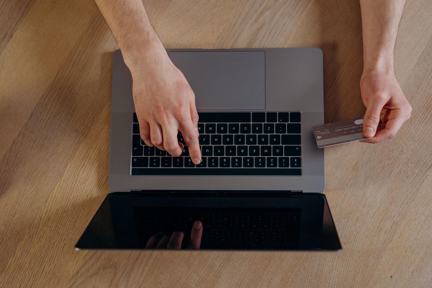 Primer plano de manos realizando una compra online con tarjeta de crédito y portátil